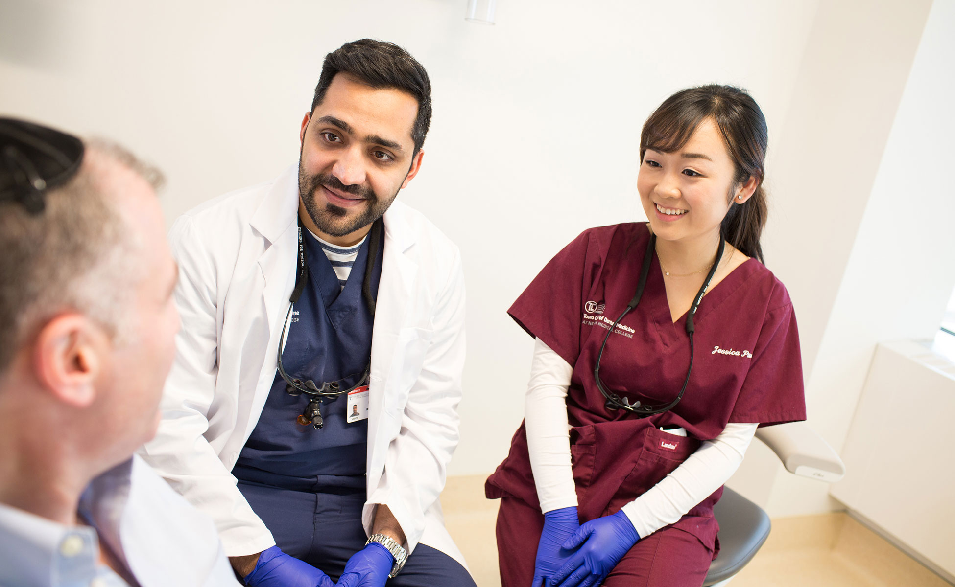 A dentist and surgeon sitting next to patient, who is reclined in chair at appointment