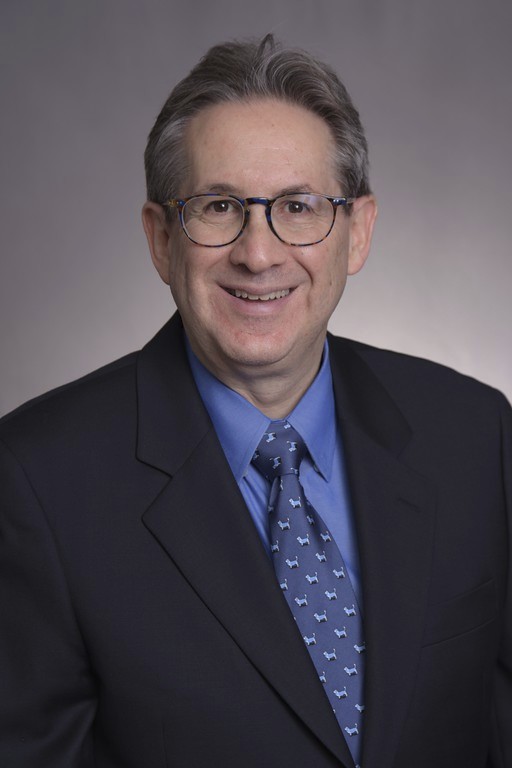 Howard Fine headshot, in black suit with blue shirt and tie