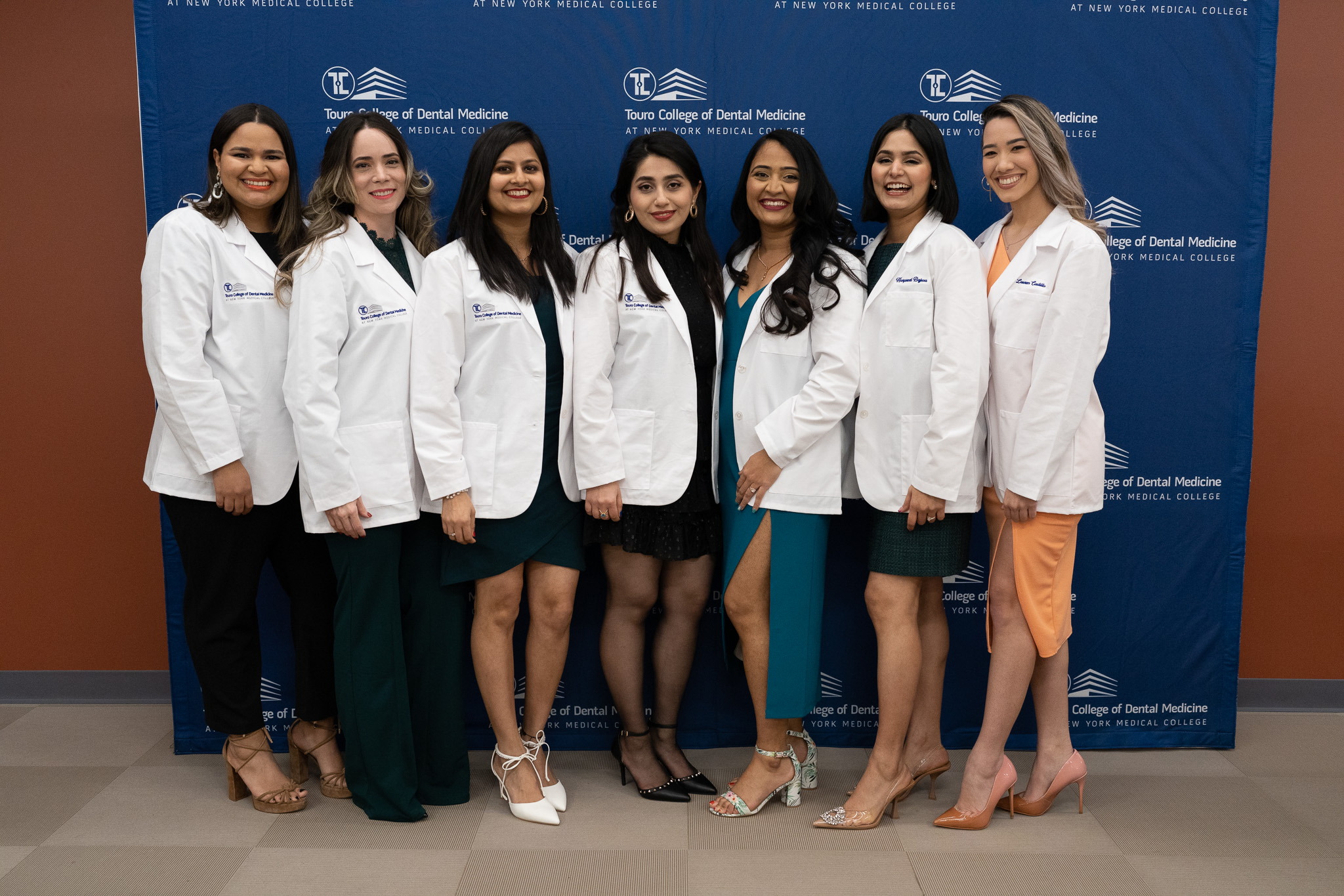 Seven students smiling together at event while wearing TCDM white coats.