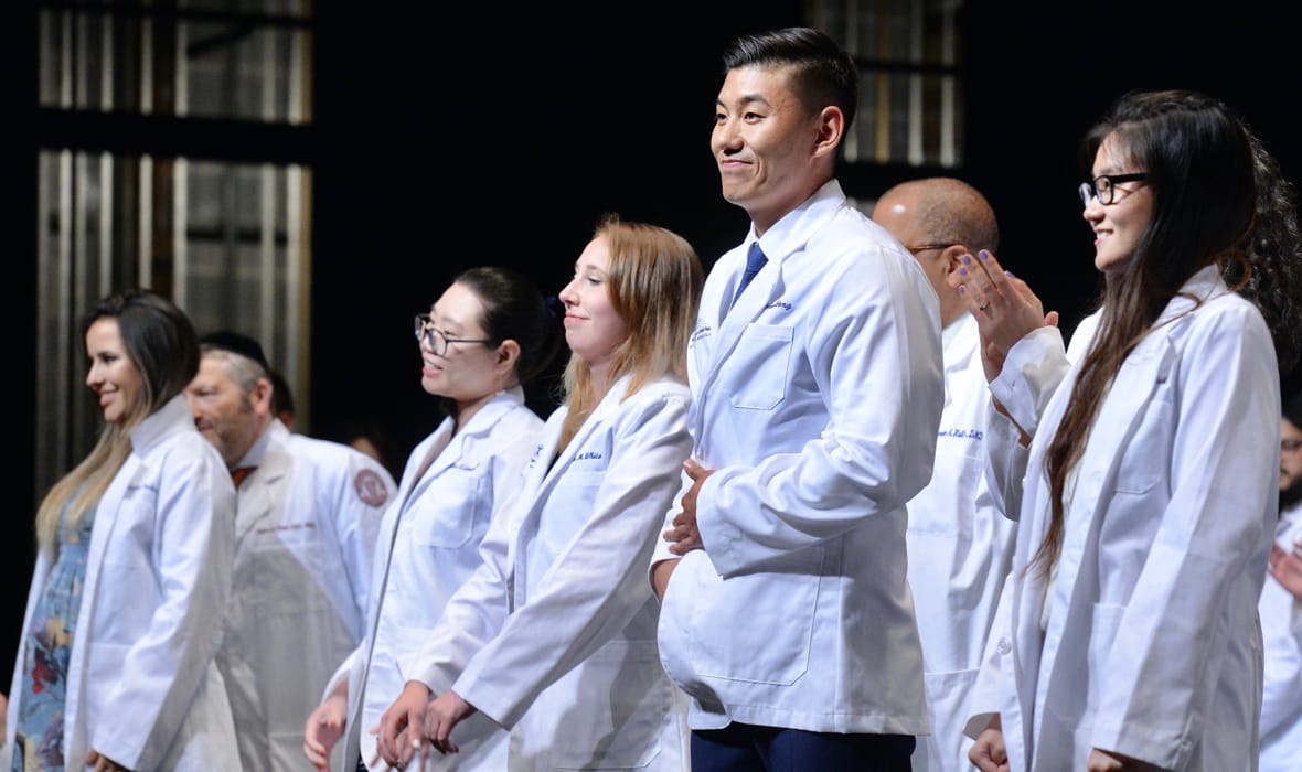 students in white coats at ceremony