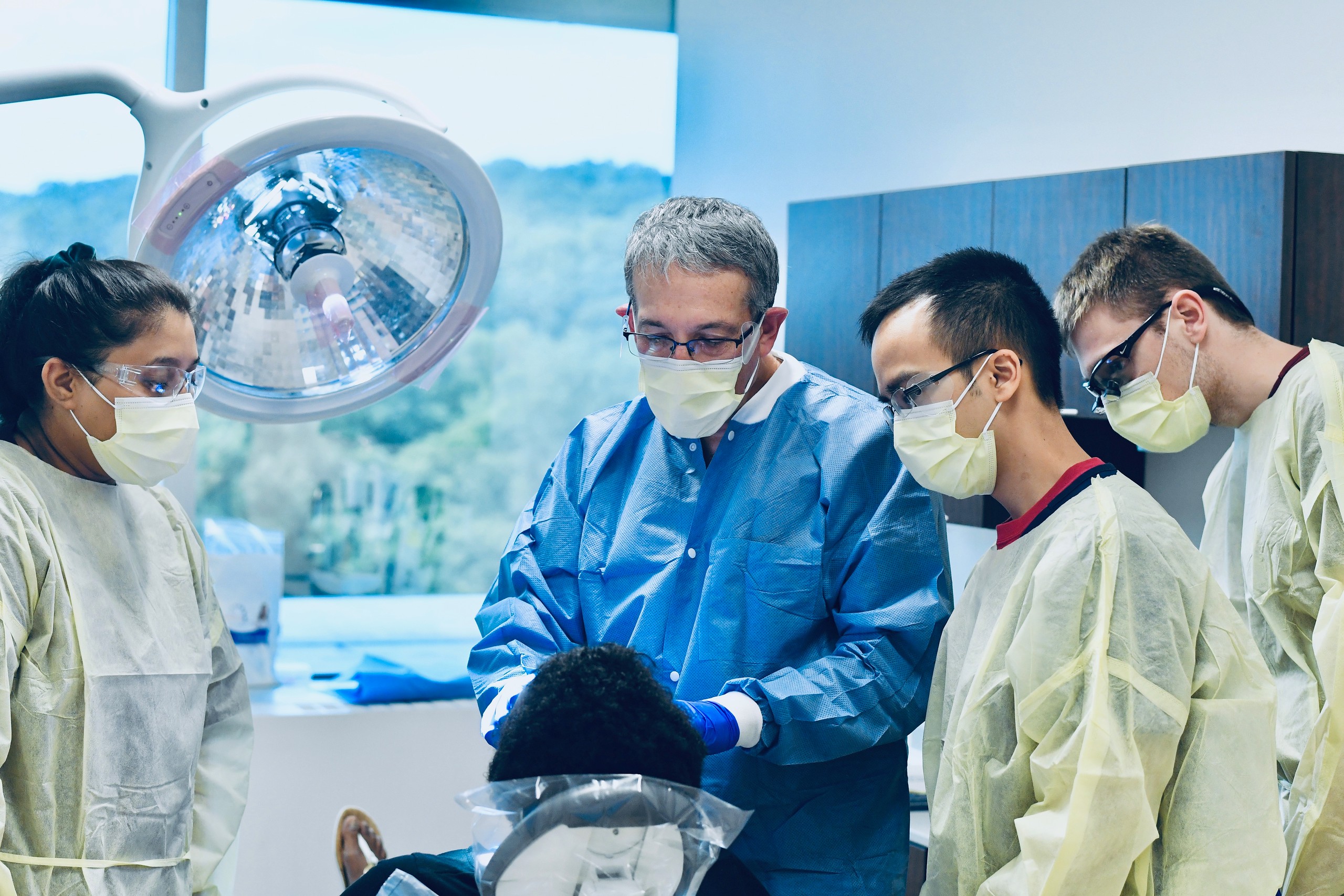 Three dental students examine a patient with their instructor. 