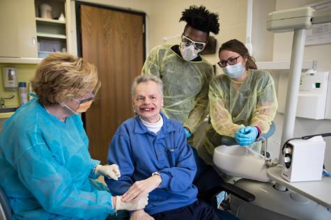 A man with a disability is being examined by a dentist and two female dental students. 