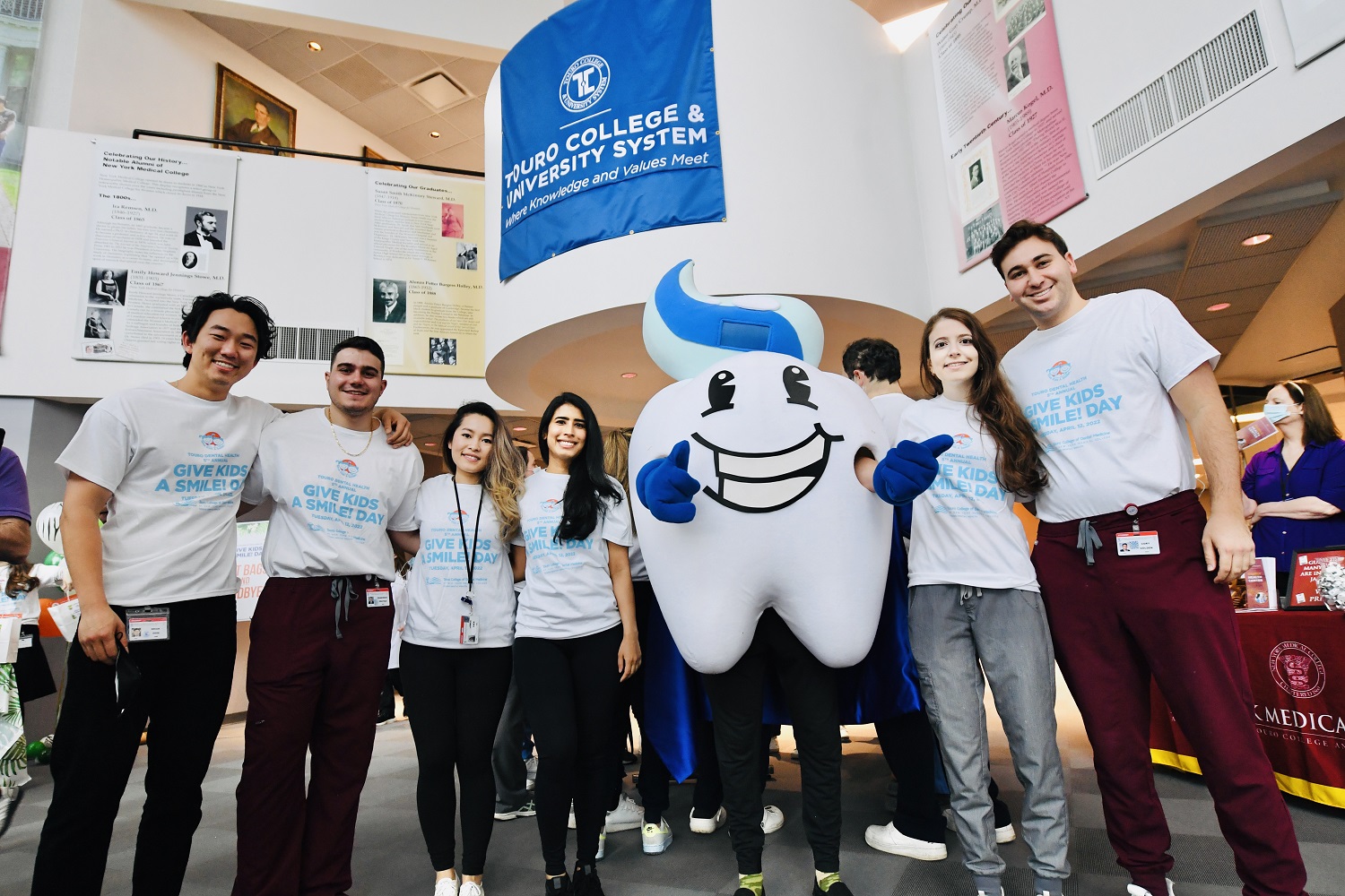 Five Touro College of Dental Medicine students stand with a person in a giant tooth costume. 