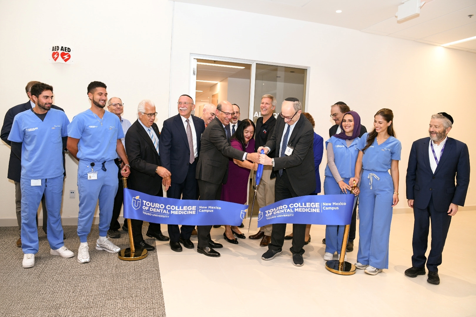 Students and faculty members using an oversized scissor to cut a ribbon by Touro\'s new dental clinic in New Mexico.