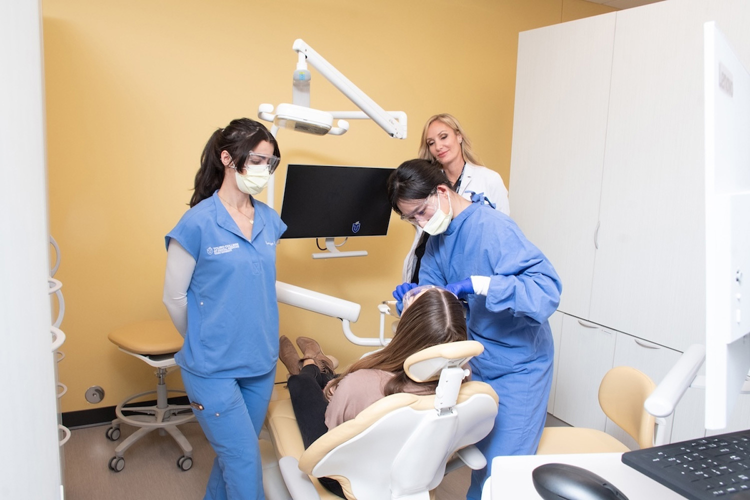 A dental student works on a patient while other students watch