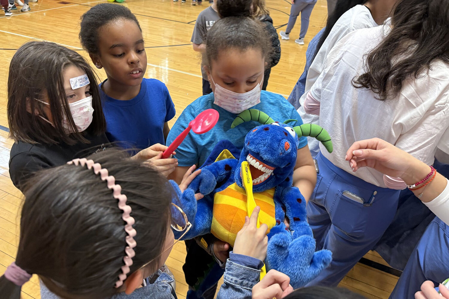 Kids use oversized toothbrushes to brush the teeth of a stuffed animal