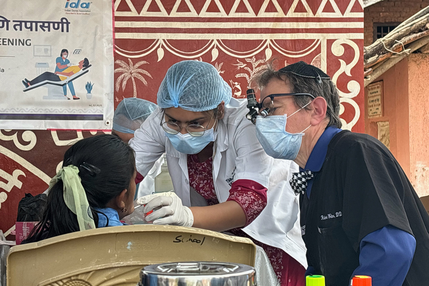 A dentist works on a patient\'s mouth while another dentist watches